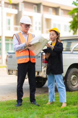 Asyalı erkek ve kadın mühendislerden oluşan bir ekip bina planlarına, inşaat mühendisliğine, iç teftişe ve konut geliştirme çalışmalarına göre bir binanın yapısını inceliyor..