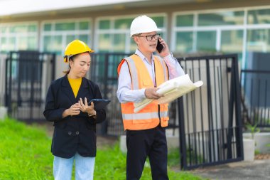 Asyalı erkek ve kadın mühendislerden oluşan bir ekip bina planlarına, inşaat mühendisliğine, iç teftişe ve konut geliştirme çalışmalarına göre bir binanın yapısını inceliyor..