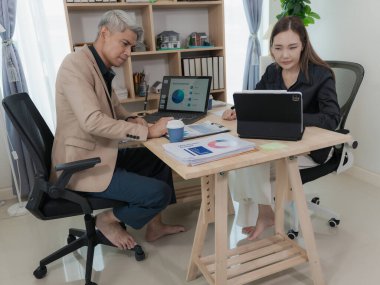 İki Asyalı iş arkadaşı dizüstü bilgisayar ve finansal belgeler üzerinde mutlu bir şekilde çalışıyor. Profesyonel erkek ve kadın. İşbirliği ve iş ortaklığı kavramı.