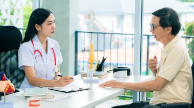 Asyalı kadın doktor son sınıf erkek hastasıyla konuşuyor. Vücut ağrısı hakkında tavsiye veriyor. Tıbbi personel tıbbi geçmişi kaydediyor..