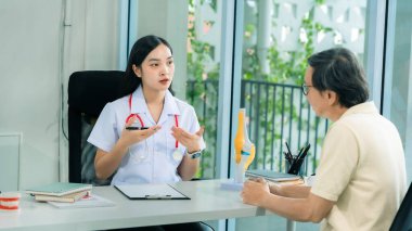 Asyalı kadın doktor son sınıf erkek hastasıyla konuşuyor. Vücut ağrısı hakkında tavsiye veriyor. Tıbbi personel tıbbi geçmişi kaydediyor..