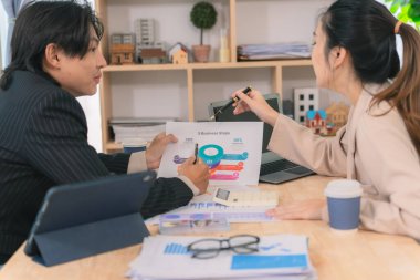 Asyalı iş çifti belge ve dizüstü bilgisayarla mali durumu tartışıyor, işletme büyüme grafiğinin ayrıntılarını anlatıyor.