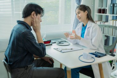 Asyalı kadın diş hekimi, diş implantı muayenesi için klinikteki erkek hastaya kanal tedavisini anlatıyor..