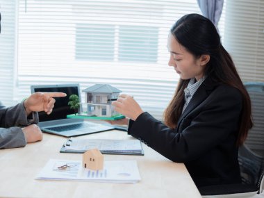 Asyalı bir kadın emlakçı ev tasarımları sunuyor, sözleşmeler imzalıyor ve konut projesindeki konut kredisi başvurularını değerlendiriyor..
