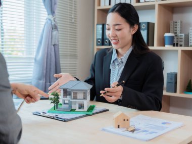 Asyalı bir kadın emlakçı ev tasarımları sunuyor, sözleşmeler imzalıyor ve konut projesindeki konut kredisi başvurularını değerlendiriyor..
