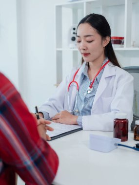 Beyaz tıbbi önlüklü ve steteskop takan genç bir Asyalı kadın doktor hastanedeki bir hastayla konuşmak için dizüstü bilgisayar kullanıyor..