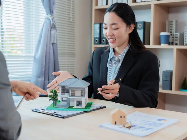 Asyalı bir kadın emlakçı ev tasarımları sunuyor, sözleşmeler imzalıyor ve konut projesindeki konut kredisi başvurularını değerlendiriyor..