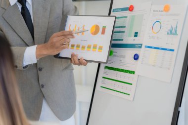 Yakın çekim bir iş beyin fırtınası sırasında hesap makineleri kullanarak muhasebe ekibinin kalem tuttuğunu ve grafiklere işaret ettiğini, pazarlama planlarını analiz ettiğini gösteriyor..