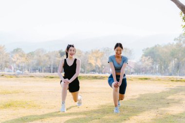 Formda iki Asyalı kadın, sağlıklı bir yaşam tarzı için parkta egzersiz yapıyor. Egzersiz yapmadan önce ısınıyor ve ısınıyorlar..