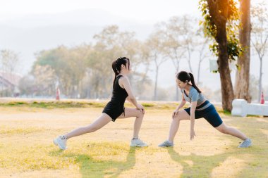 Formda iki Asyalı kadın, sağlıklı bir yaşam tarzı için parkta egzersiz yapıyor. Egzersiz yapmadan önce ısınıyor ve ısınıyorlar..