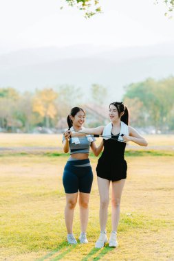 Formda iki Asyalı kadın, sağlıklı bir yaşam tarzı için parkta egzersiz yapıyor. Egzersiz yapmadan önce ısınıyor ve ısınıyorlar..