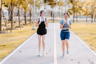 Sağlıklı bir yaşam tarzını geliştirmek için parkta koşan iki sağlıklı Asyalı kadın görülüyor..