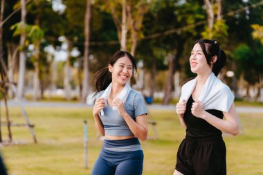 Sağlıklı bir yaşam tarzını geliştirmek için parkta koşan iki sağlıklı Asyalı kadın görülüyor..