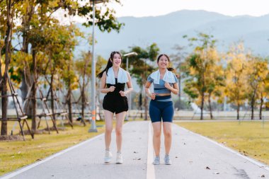 Sağlıklı bir yaşam tarzını geliştirmek için parkta koşan iki sağlıklı Asyalı kadın görülüyor..