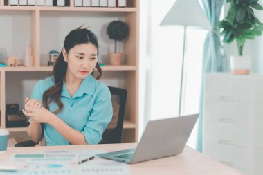 Asyalı bir kadın muhasebeci masasında çalışırken şiddetli bir ağrı yaşadı. Bu da kötü bir duruş ya da uzun süre oturma durumu olduğunu gösteriyor..