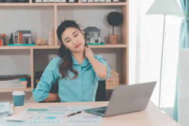 Asyalı bir kadın muhasebeci masasında çalışırken şiddetli bir ağrı yaşadı. Bu da kötü bir duruş ya da uzun süre oturma durumu olduğunu gösteriyor..