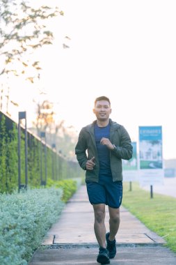 Genç bir Asyalı sabah bir parkta dışarıda koşuyor. Sağlık için egzersiz kavramı tasvir edilmiştir..