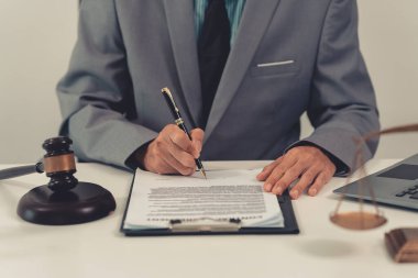 Yakından bakınca, elinde küçük bir tokmakla ofisinde oturan bir avukat görülüyor. Mahkeme masasına vurduğu için. Masasında adalet terazisi var..