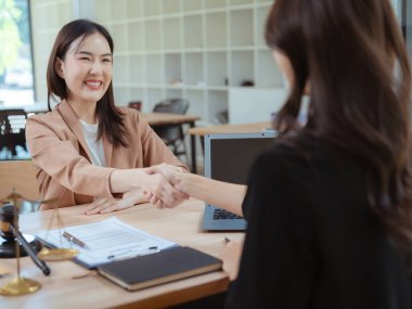 Bir iş kadını ve kadın avukatın, bir ofis toplantısında sözleşme imzaladıktan sonra el sıkışması birlik ve işbirliğini simgeler..