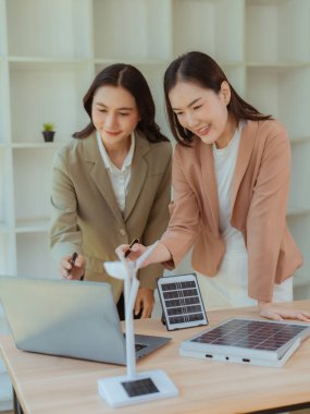 İki Asyalı iş kadını, çevre dostu enerji üretmek için temiz enerji iş konseptini göstermek amacıyla güneş panelleri tutuyor.