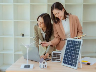İki Asyalı iş kadını, çevre dostu enerji üretmek için temiz enerji iş konseptini göstermek amacıyla güneş panelleri tutuyor.