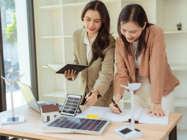 İki Asyalı iş kadını, çevre dostu enerji üretmek için temiz enerji iş konseptini göstermek amacıyla güneş panelleri tutuyor.