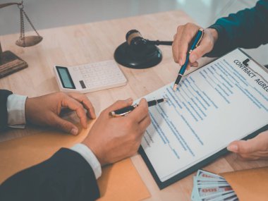 A male lawyer or judge is consulting with or discussing various contractual documents with a client to assist them. This is a concept related to law.