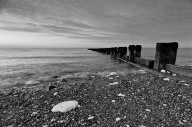 Şafak vakti Bridlington 'ın kuzey sahilindeki Groynes' in siyah beyaz fotoğrafı, dalgaların hareket bulanıklığı.
