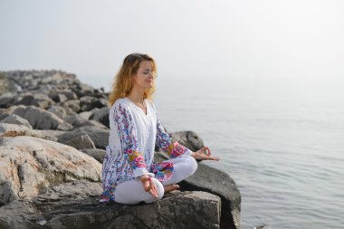 Genç kadın bir kayalık okyanus kıyısında yoga yaparken