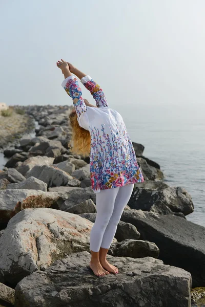 Giovane donna che fa yoga su una riva rocciosa dell'oceano — Foto Stock