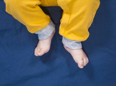 Mavi arka planda sarı pantolonlu bebek bacakları. Çıplak ayaklar