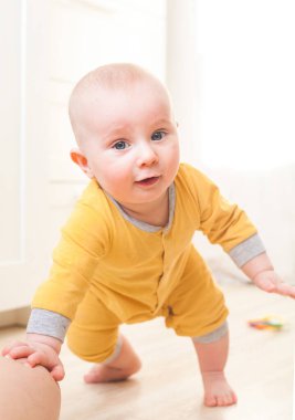Yedi aylık sarı elbiseli çocuk kalkmaya çalışıyor.