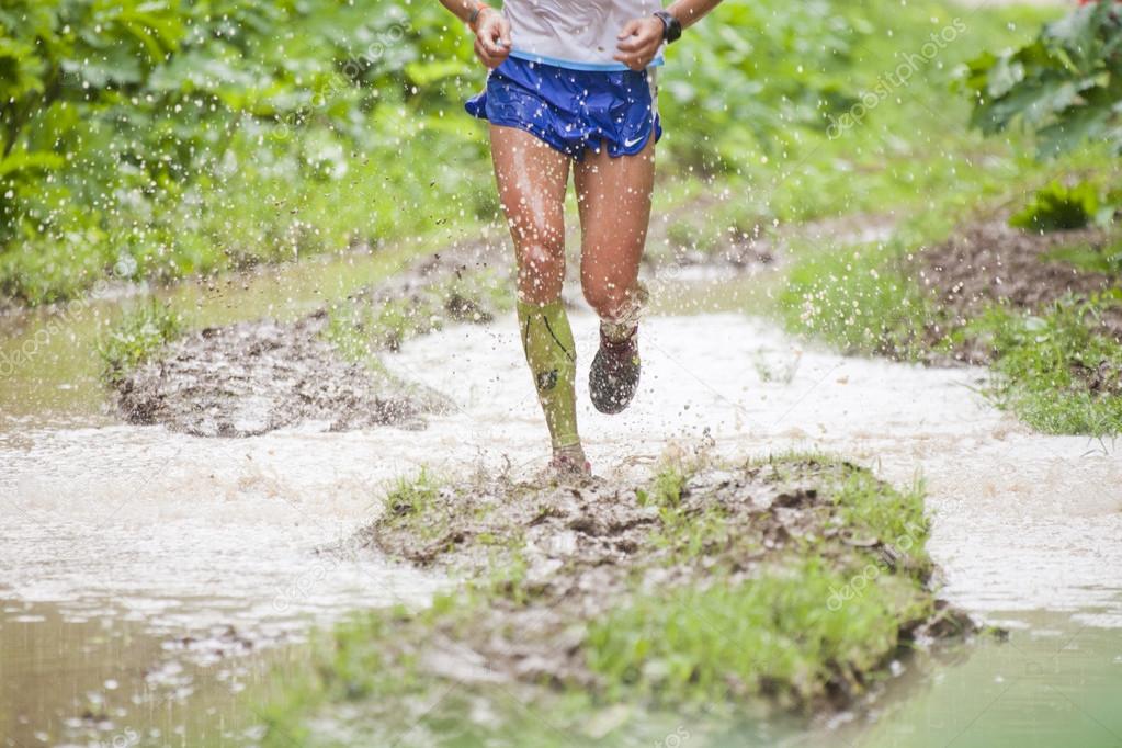 Athlete's legs running through puddles. Dirt and water splashes