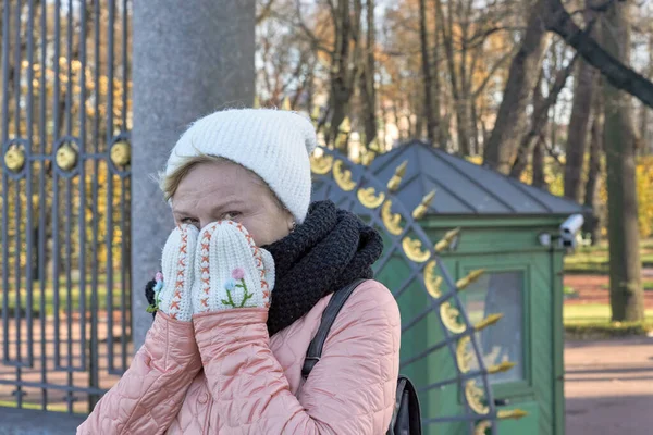 一个女人在夏园格子的背景下 用羊毛手套捂住她冰冷的脸 — 图库照片