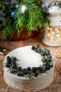 Yeni yıl masasında el feneri ve ladin dallarıyla süslenmiş böğürtlenlerle süslenmiş büyük yuvarlak bir pasta. Dikey çerçeve