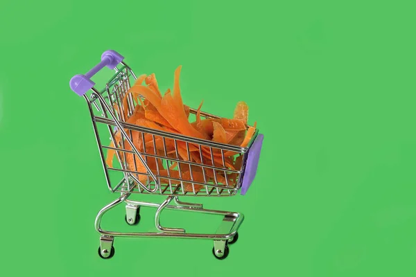 Sinaasappel Pelende Wortelen Een Supermarkt Trolley Een Groene Achtergrond Close — Stockfoto