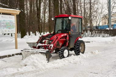 Büyük kovalı kırmızı traktör şehir parkındaki karı kaldırıyor.