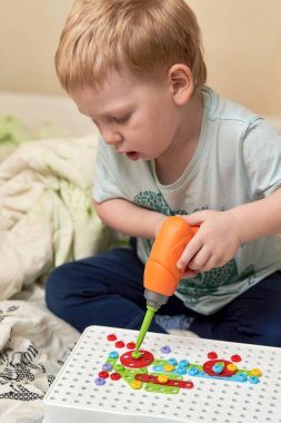 Küçük çocuk inşaatçıda aletlerle oynuyor.