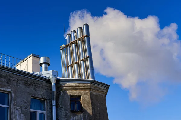 Mnoho komínů na střeše starého domu kouří proti modré obloze — Stock fotografie