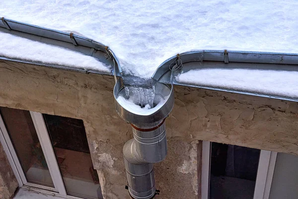 Eski bir evin karla kaplı çatısı. Donmuş suyla su gideri var.