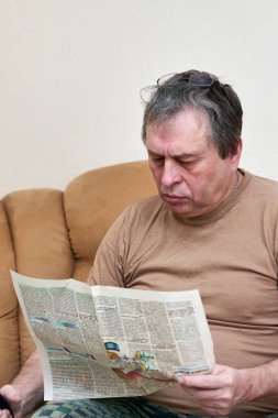 Kanepede oturan yaşlı bir adam gazetede gazete okuyor..