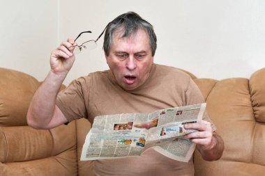 Kanepede oturan yaşlı bir adam gazetede gazete okuyor..