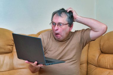 Devani 'nin üzerinde oturacak yaşta bir adam haberlere dizüstü bilgisayarla bakıyor..