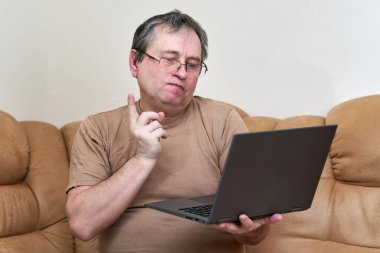 Devani 'nin üzerinde oturacak yaşta bir adam haberlere dizüstü bilgisayarla bakıyor..