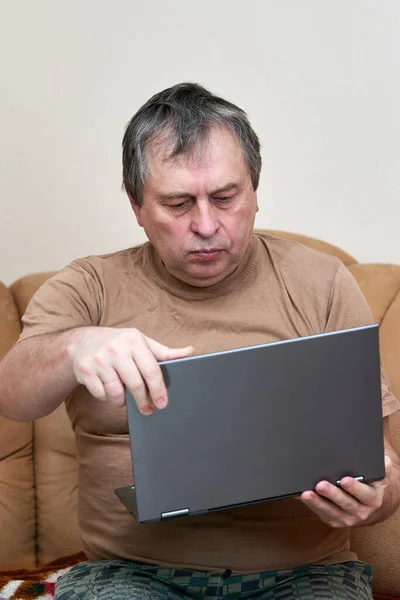 Ein Mann im Alter, der auf Devani sitzt, blättert auf einem Laptop durch die Nachrichten. — Stockfoto