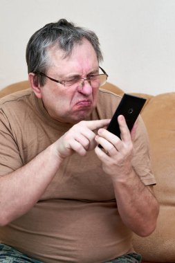 Kanepede oturan yaşlı vatandaş aleti anlıyor, akıllı telefonda ustalaşıyor.