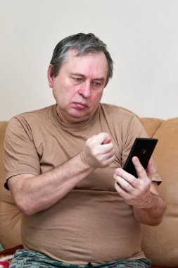 Kanepede oturan yaşlı vatandaş aleti anlıyor, akıllı telefonda ustalaşıyor.