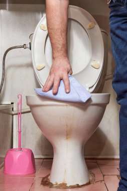 Paçavralı bir el kirli bir klozetin kenarını siler.