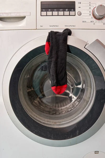 A clean black sock hangs on the door of the washing machine