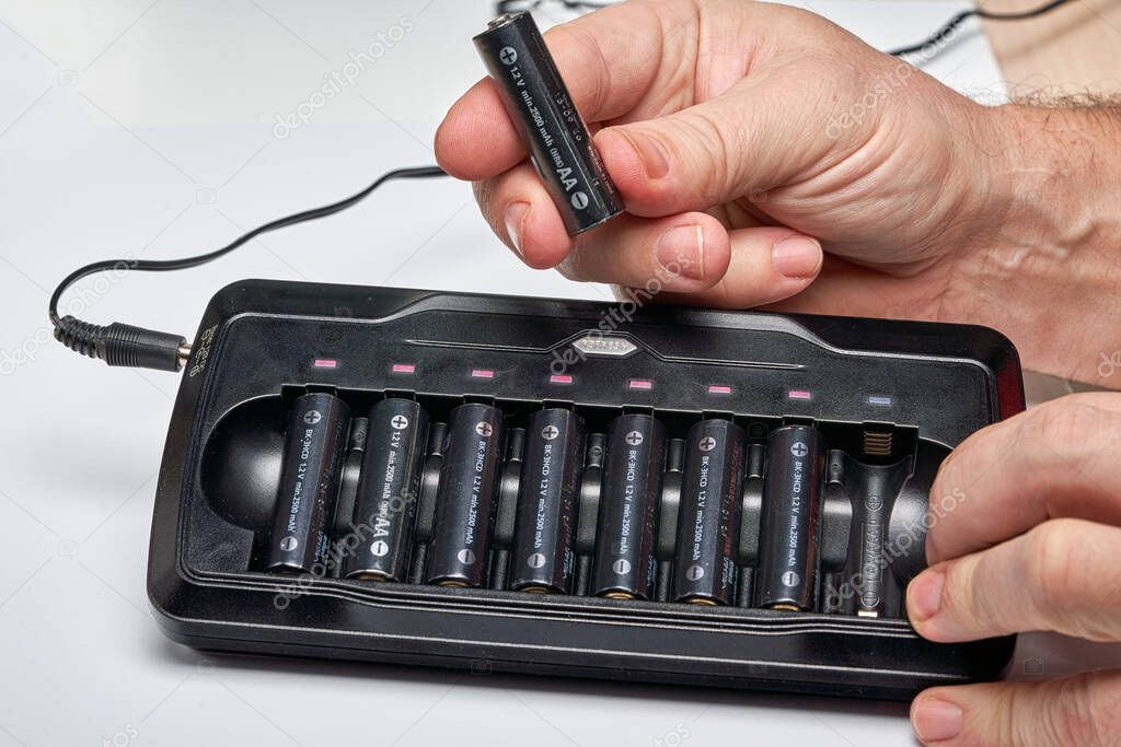 Hands insert AA batteries into black long charger